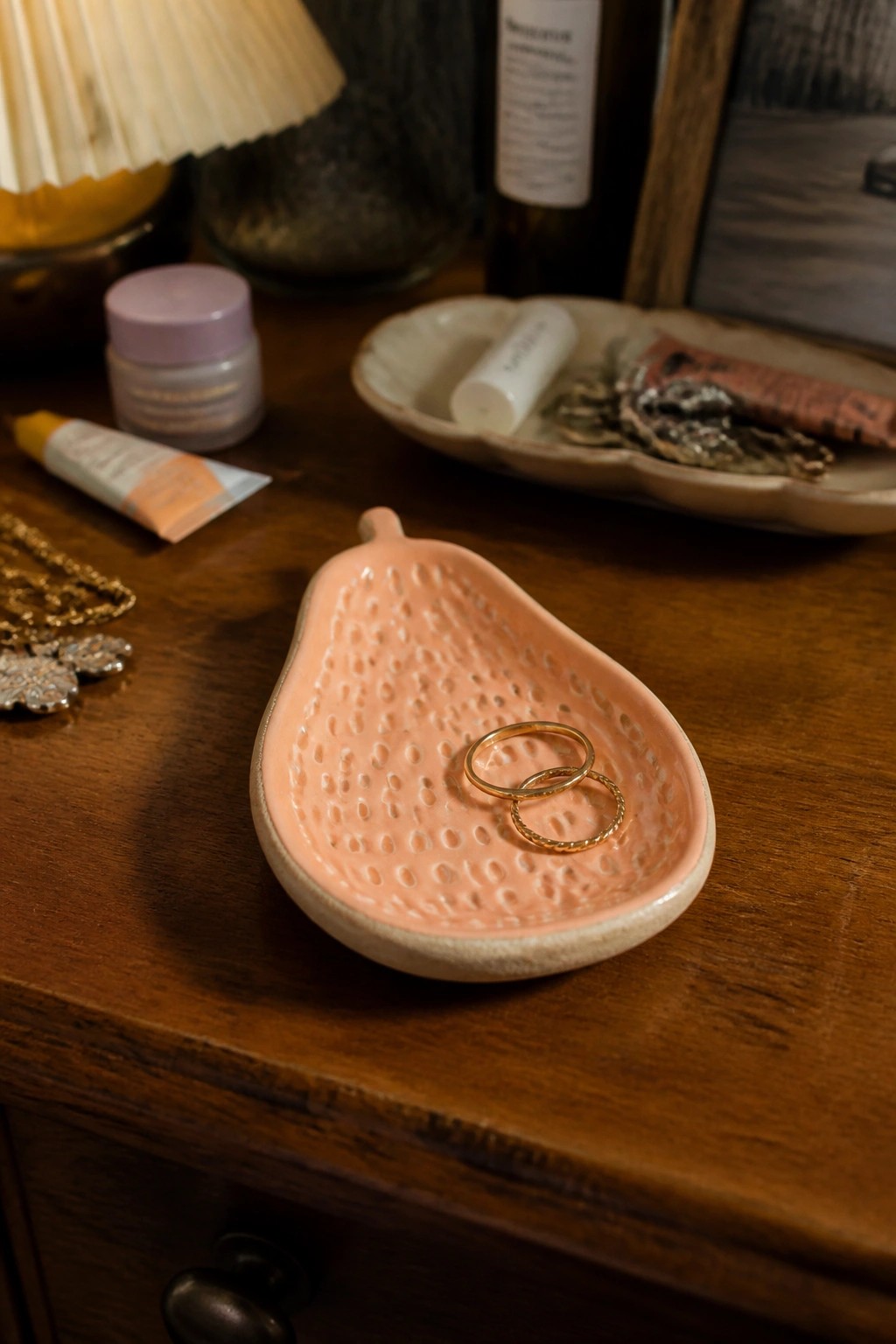 Pink strawberry-shaped ceramic dish holding two gold rings on wooden dresser.