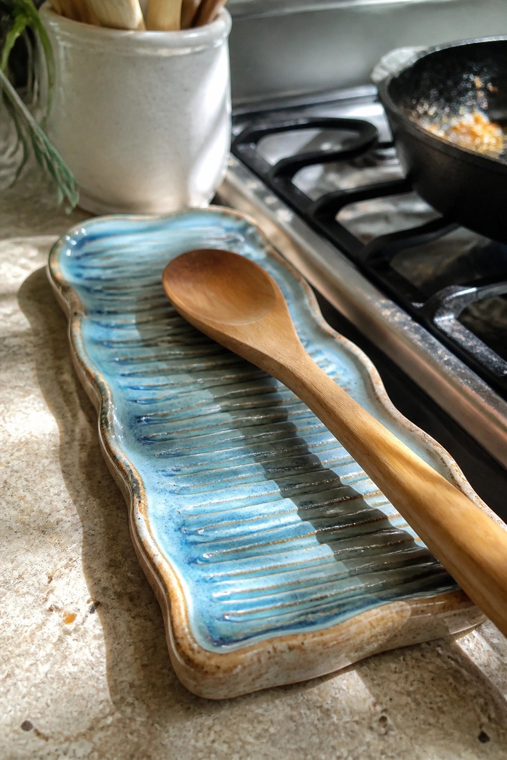 Wooden spoon on blue ridged ceramic tray beside gas stove
