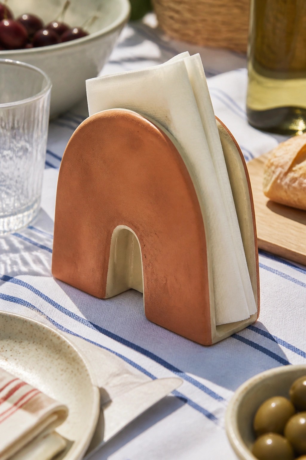 Terracotta arch napkin holder with white napkins on blue striped tablecloth.