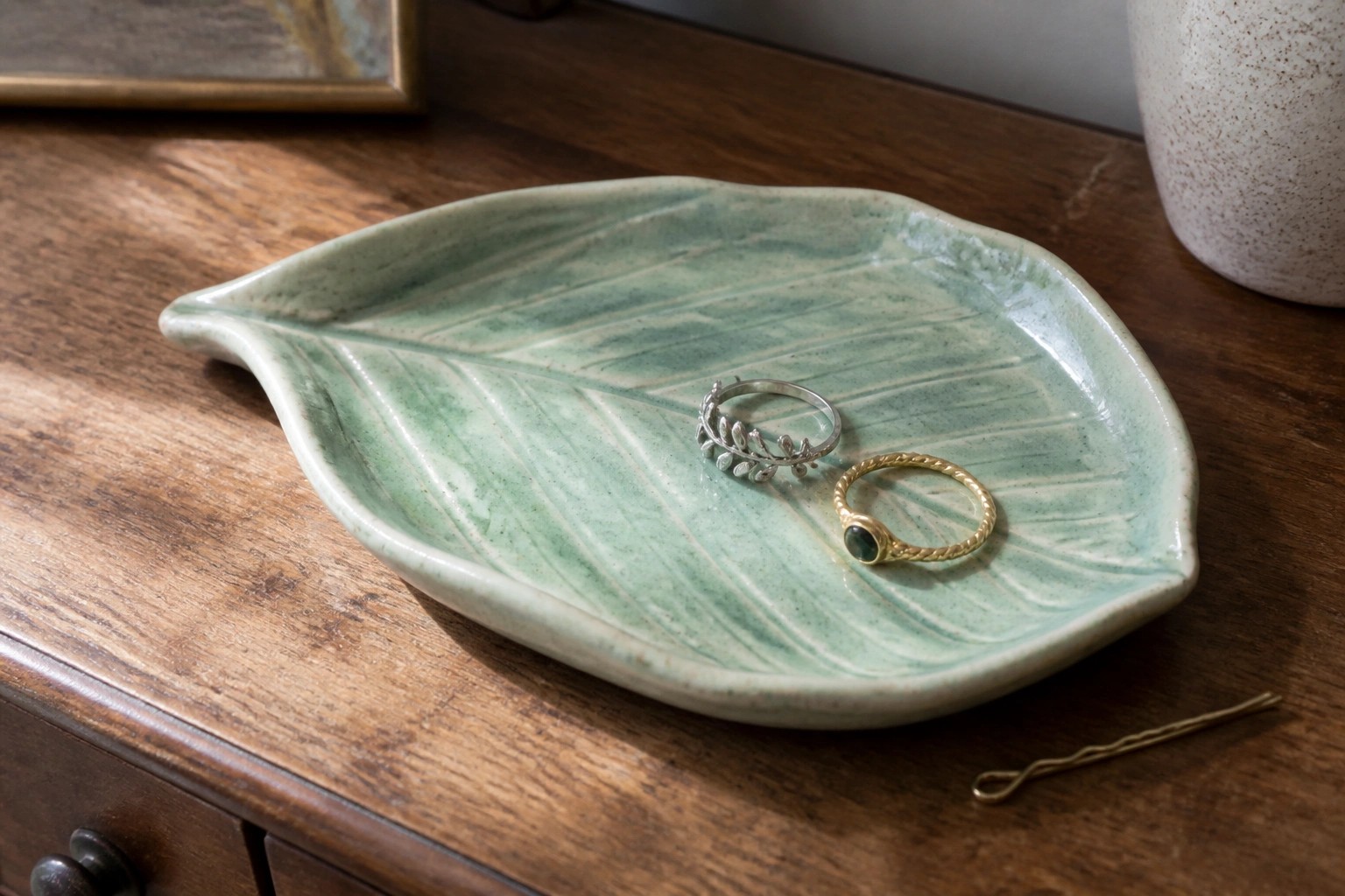 Green leaf-shaped ceramic dish holding three gold rings on wooden table