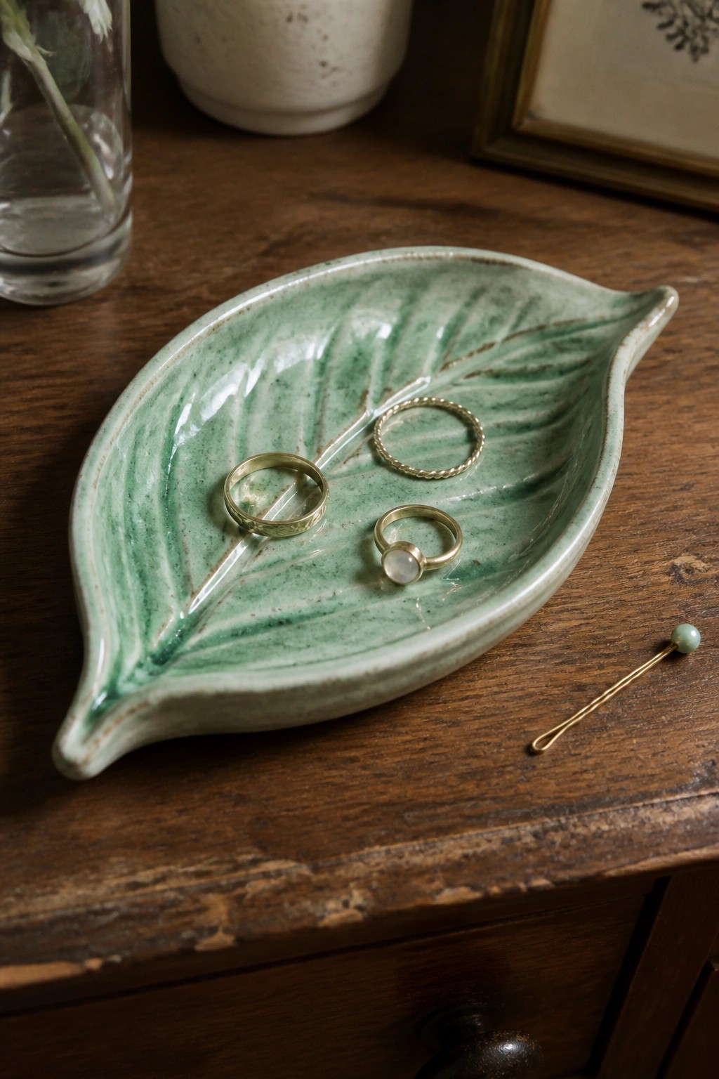 Green leaf-shaped ceramic dish holding three gold rings on wooden table