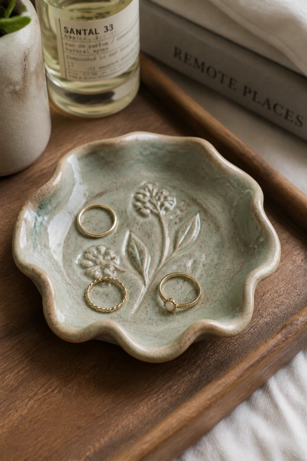 Green ceramic dish with floral design holding three gold rings on wood tray