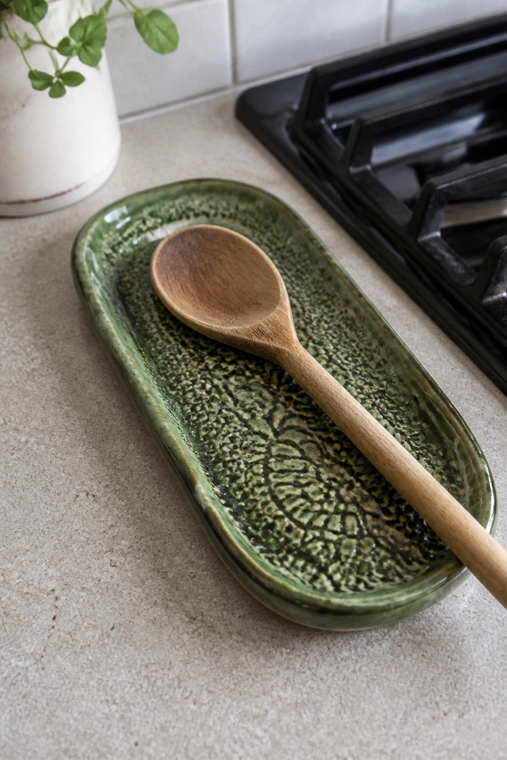 Green ceramic dish holding wooden spoon on kitchen counter near black stove
