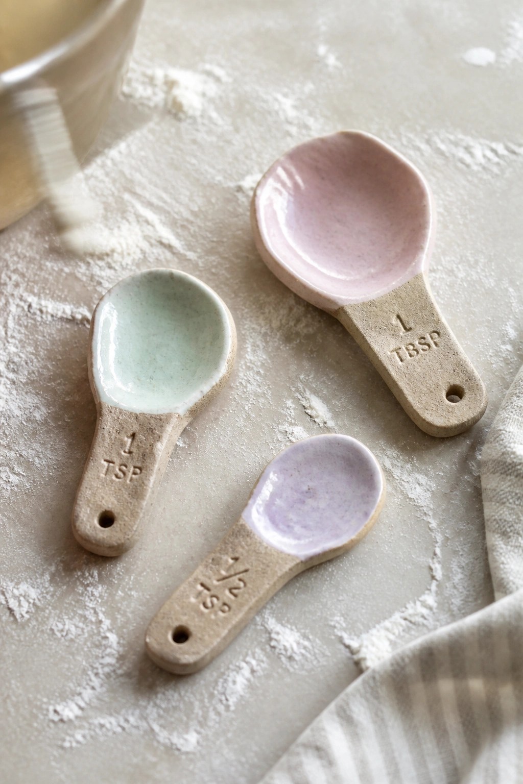 Pastel ceramic measuring spoons on a flour-dusted baking surface with bowl