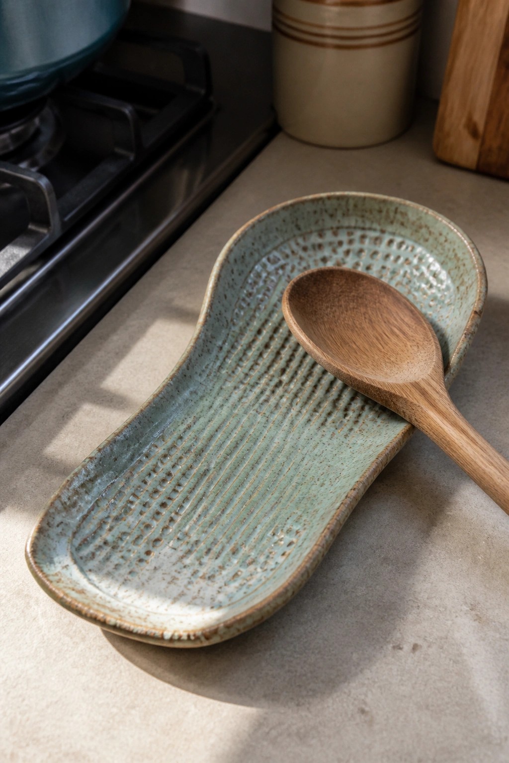 Wooden spoon on textured light blue-green ceramic tray near stove
