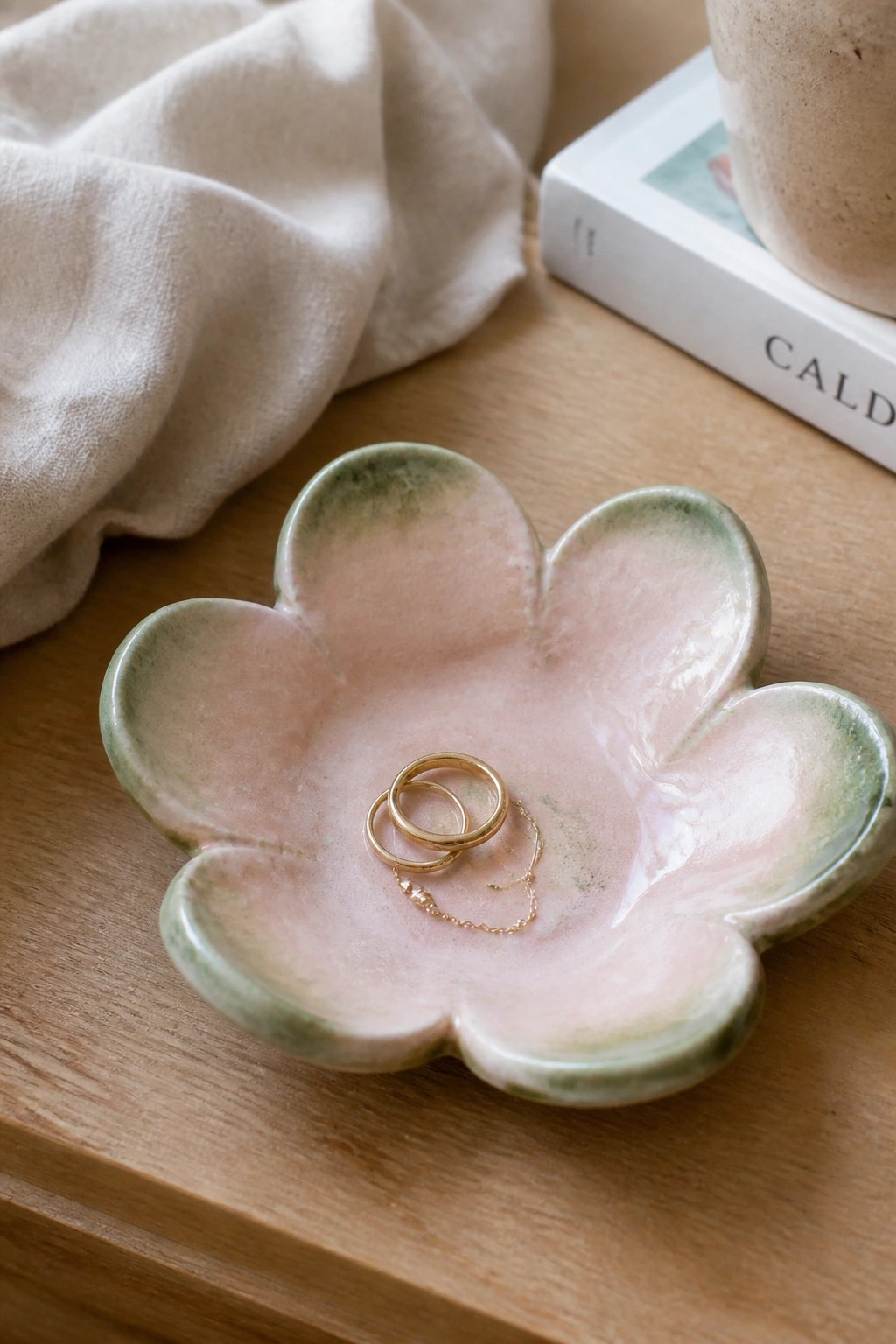 Flower-shaped pink ceramic dish holding gold rings and chain on wooden table