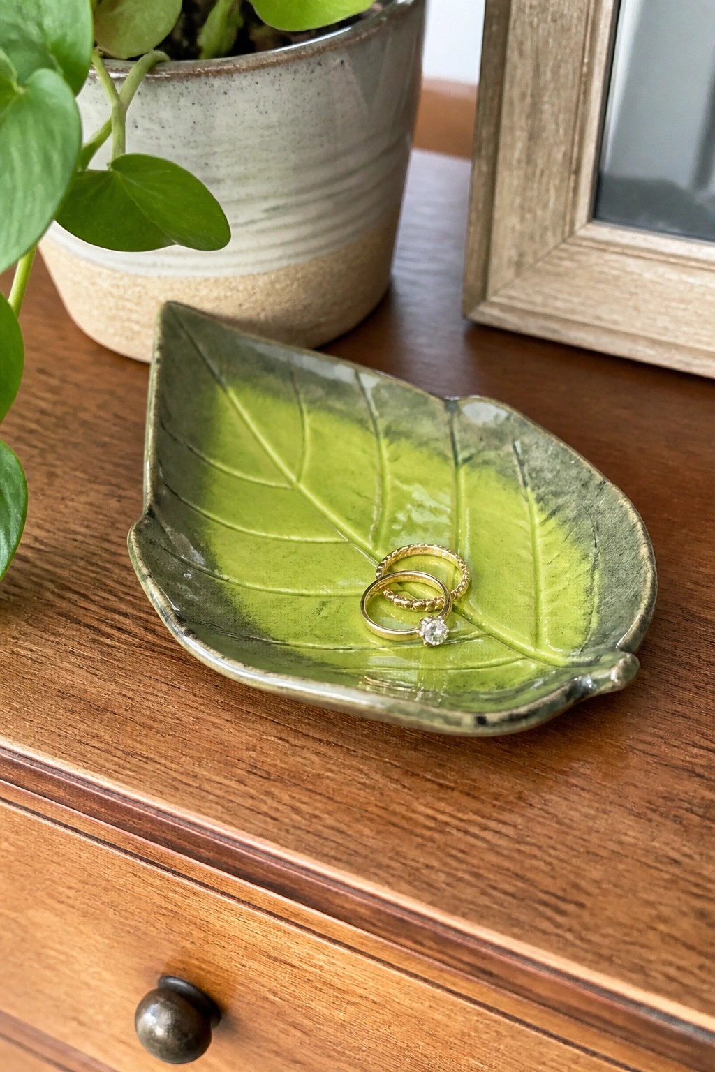 Green leaf-shaped ceramic dish holding two gold rings on wooden table