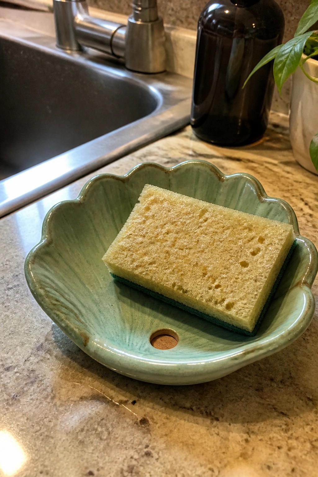 Yellow sponge in green scalloped ceramic bowl with drain hole on marble counter