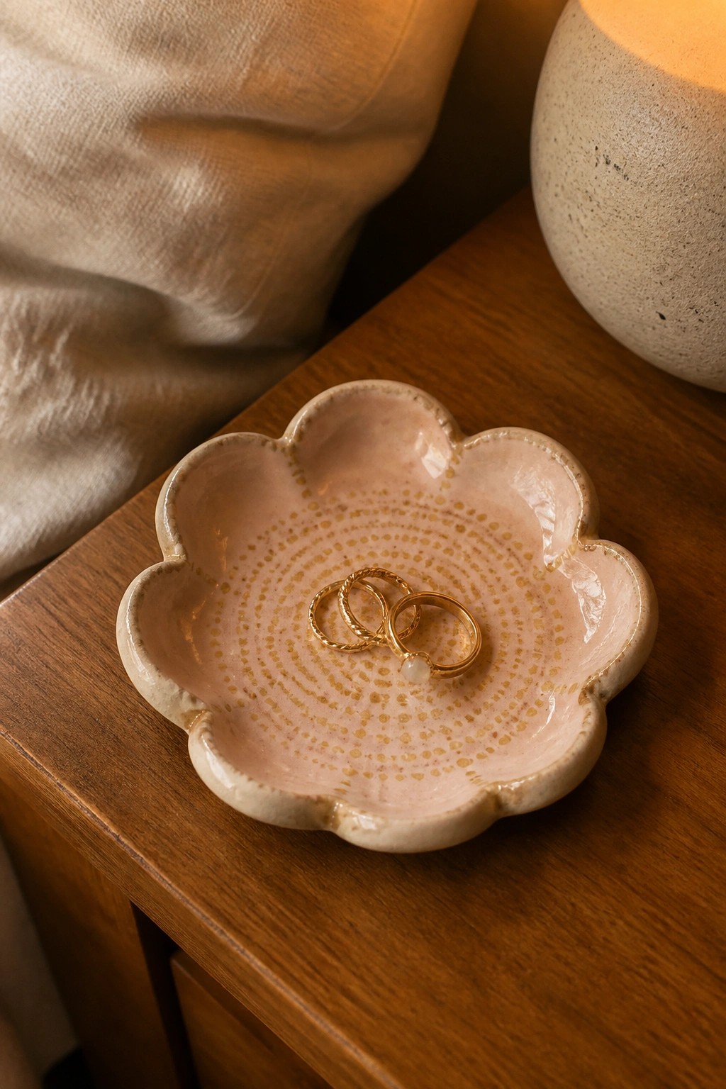 Pink flower-shaped ceramic dish holding gold rings on wooden table