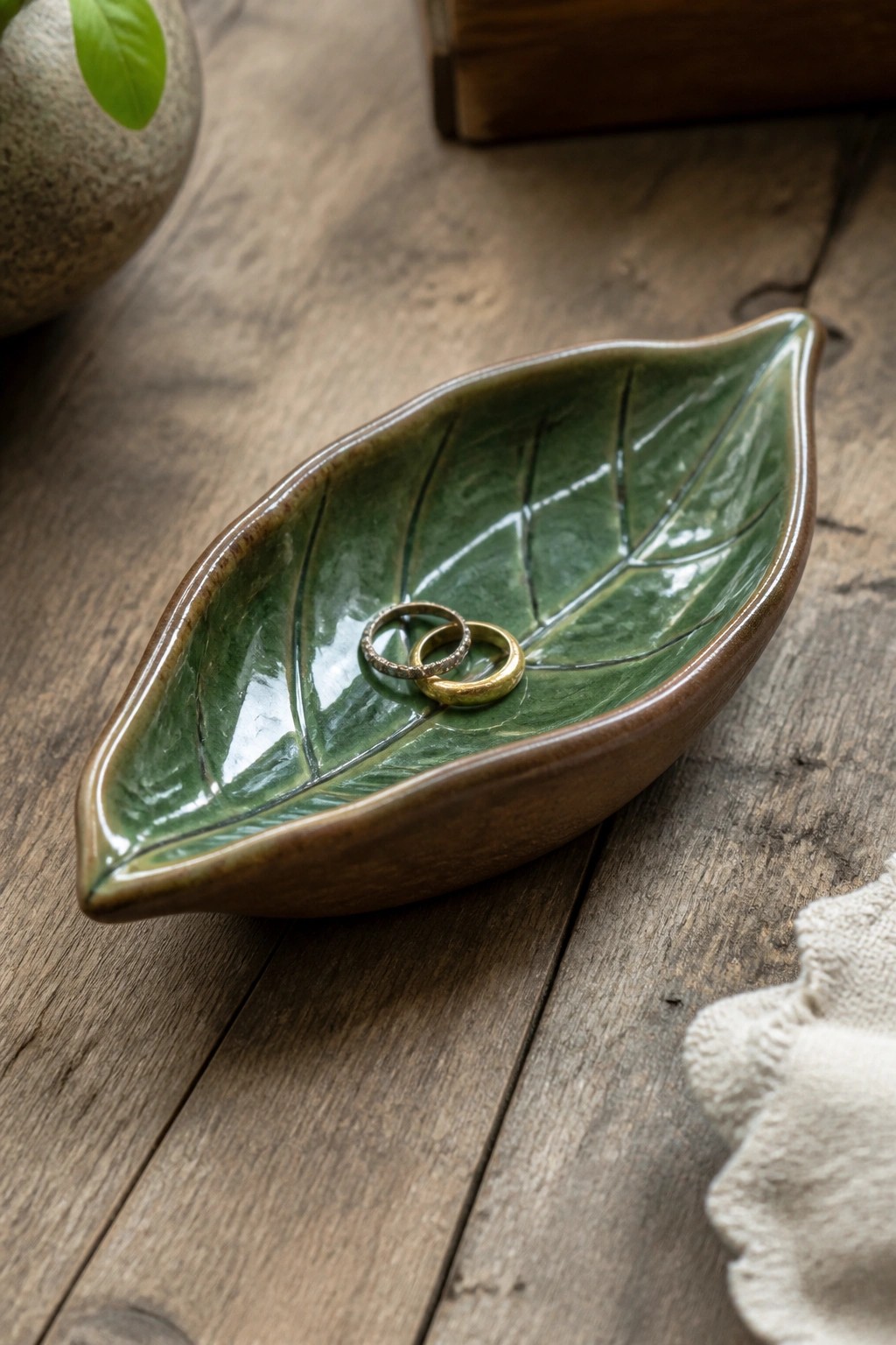 Green leaf-shaped ceramic dish holding two gold rings on wooden table.