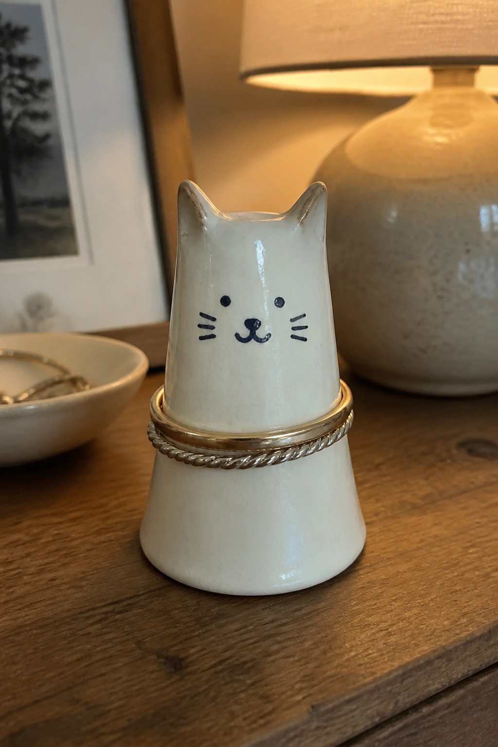White ceramic cat ring holder with gold and silver rings on wooden table.