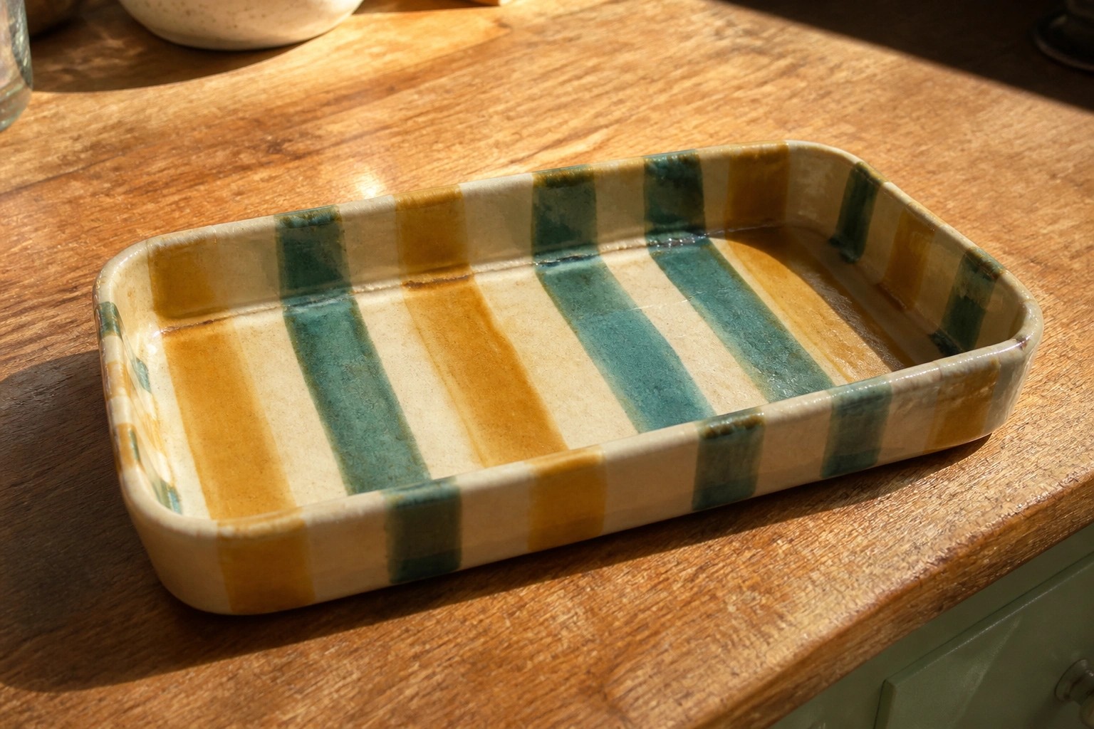 A rectangular ceramic tray with yellow and teal horizontal stripes sits on a wooden table.