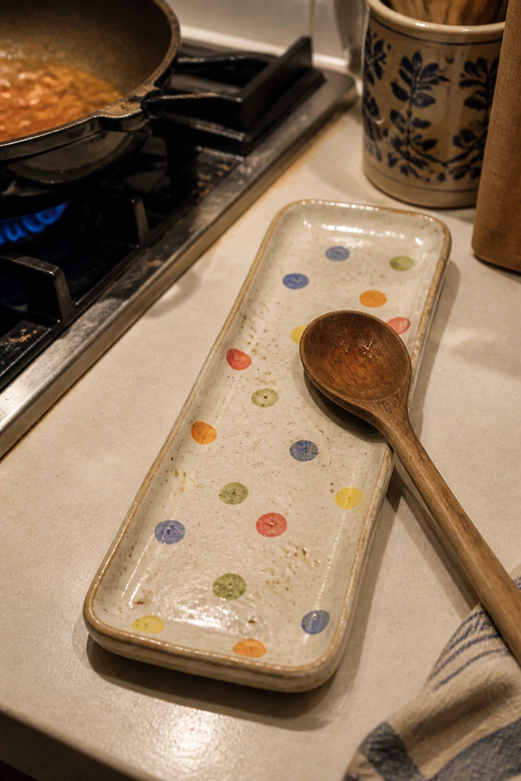 Polka-dotted ceramic tray with wooden spoon beside pan on gas stove