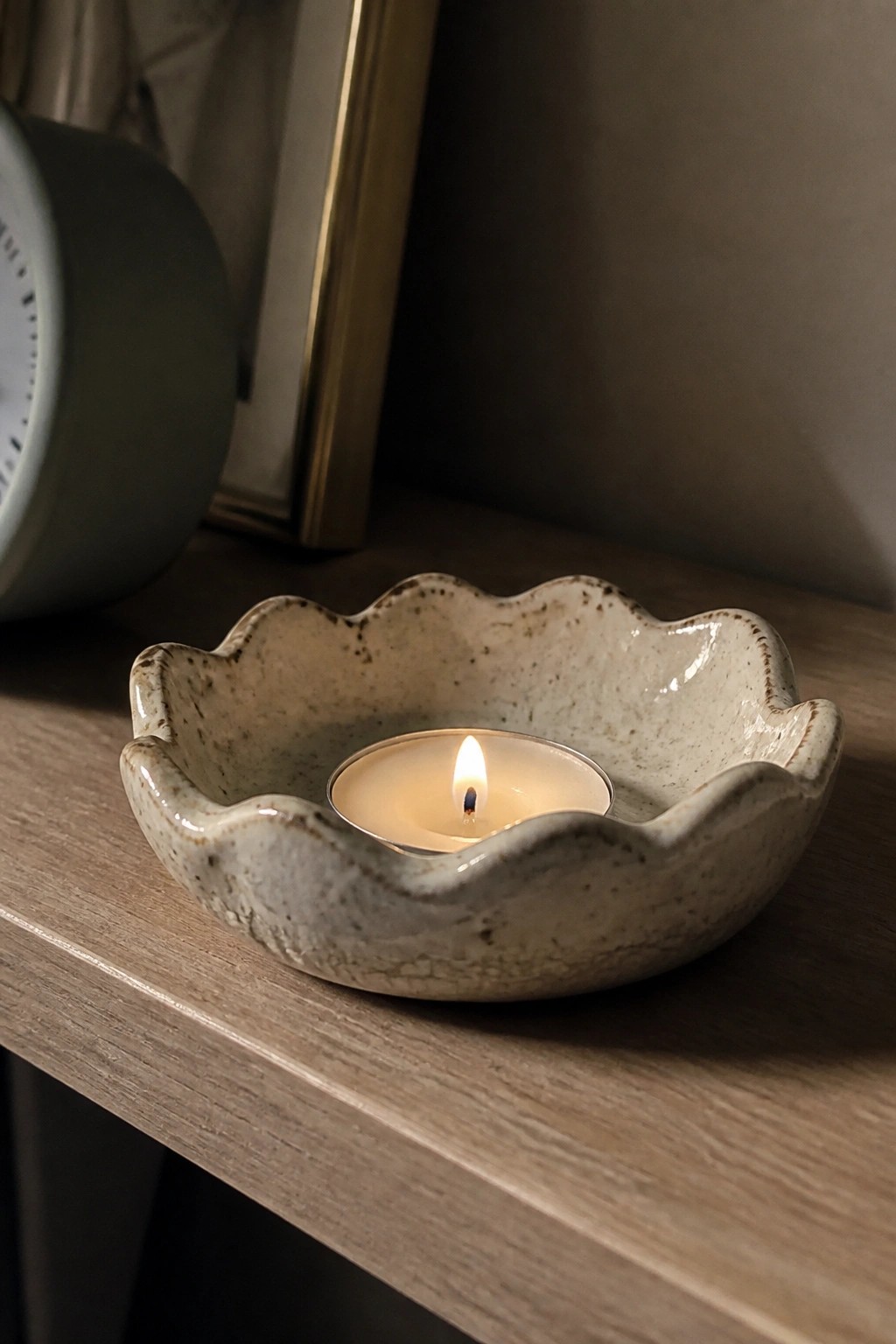 Lit tea light in a scalloped speckled ceramic bowl on wooden surface.