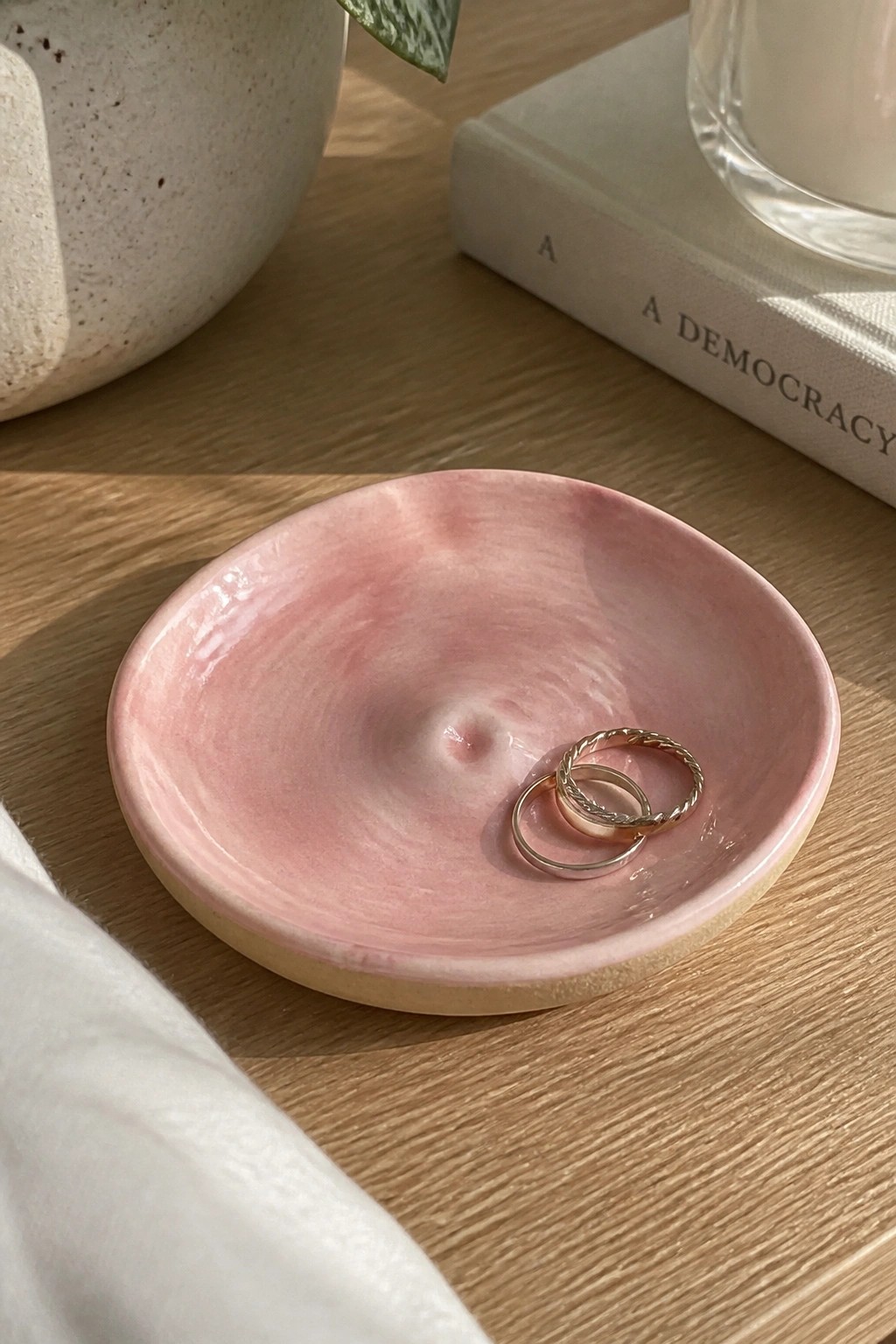 Pink marbled ceramic dish holding two gold rings on wooden table