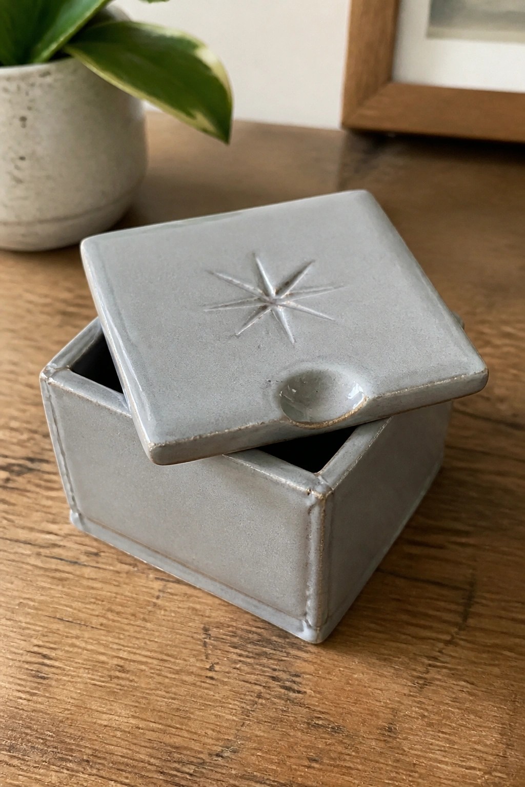 Square gray ceramic box with star design on lid, slightly open on wood table