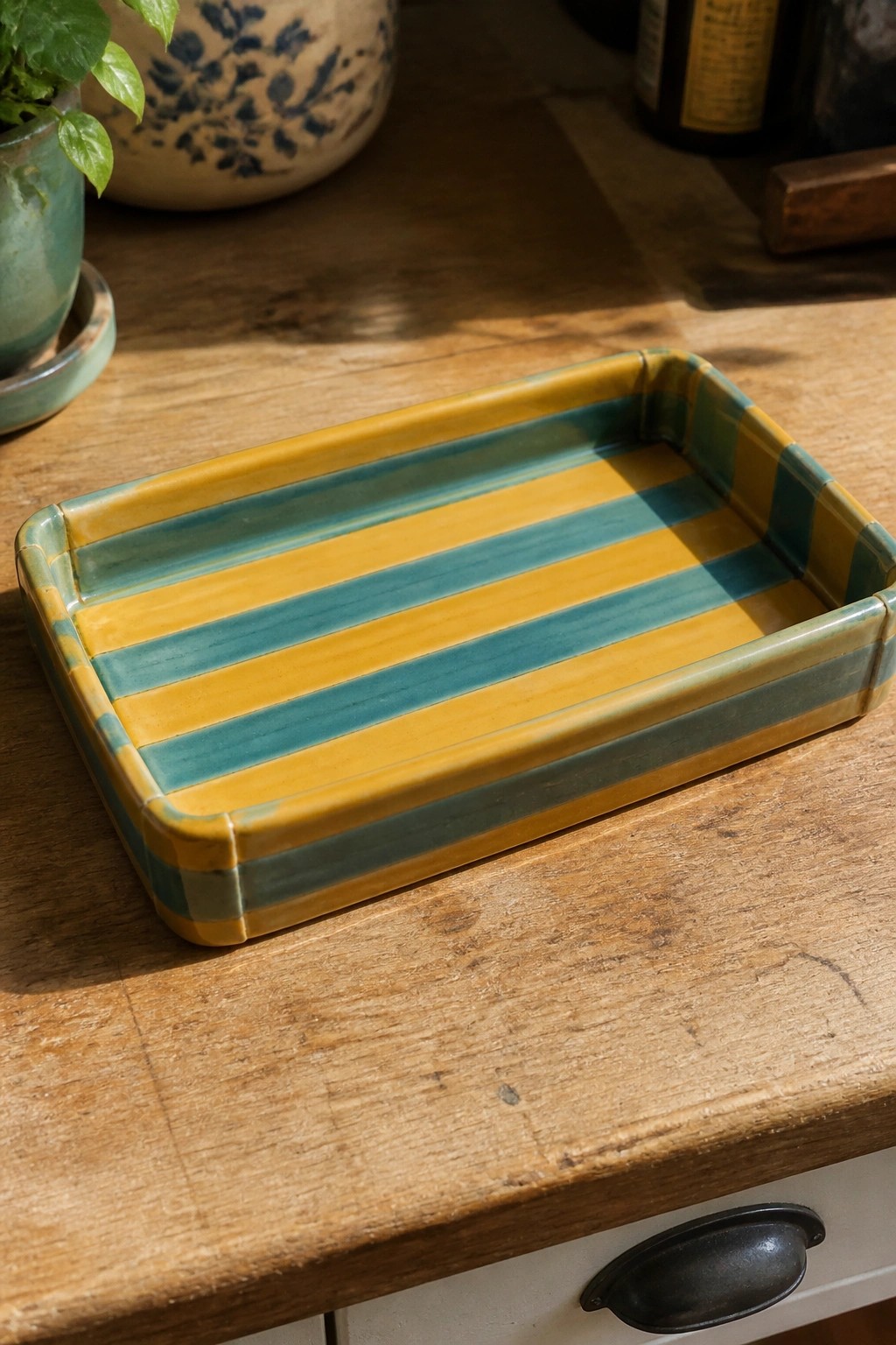 A rectangular ceramic tray with yellow and teal horizontal stripes sits on a wooden table.