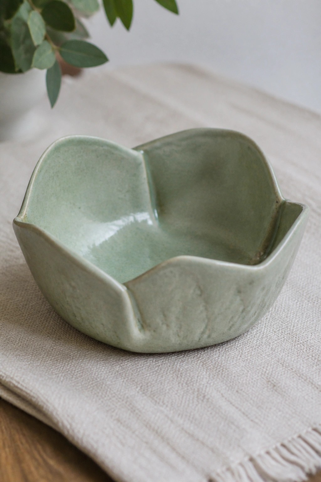 Light green ceramic bowl with wavy edges on beige woven cloth.