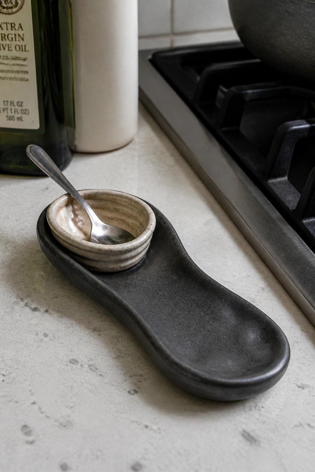 Small speckled bowl with spoon on dark ceramic tray near stovetop