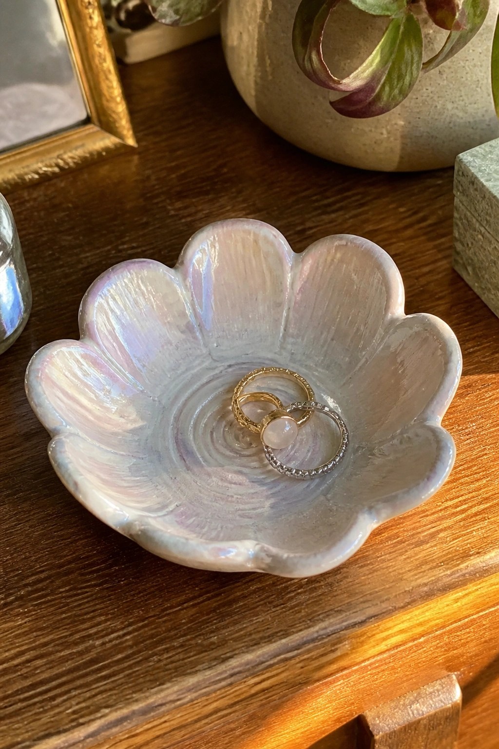 Iridescent pink-white flower-shaped ceramic bowl holding three rings on wooden table