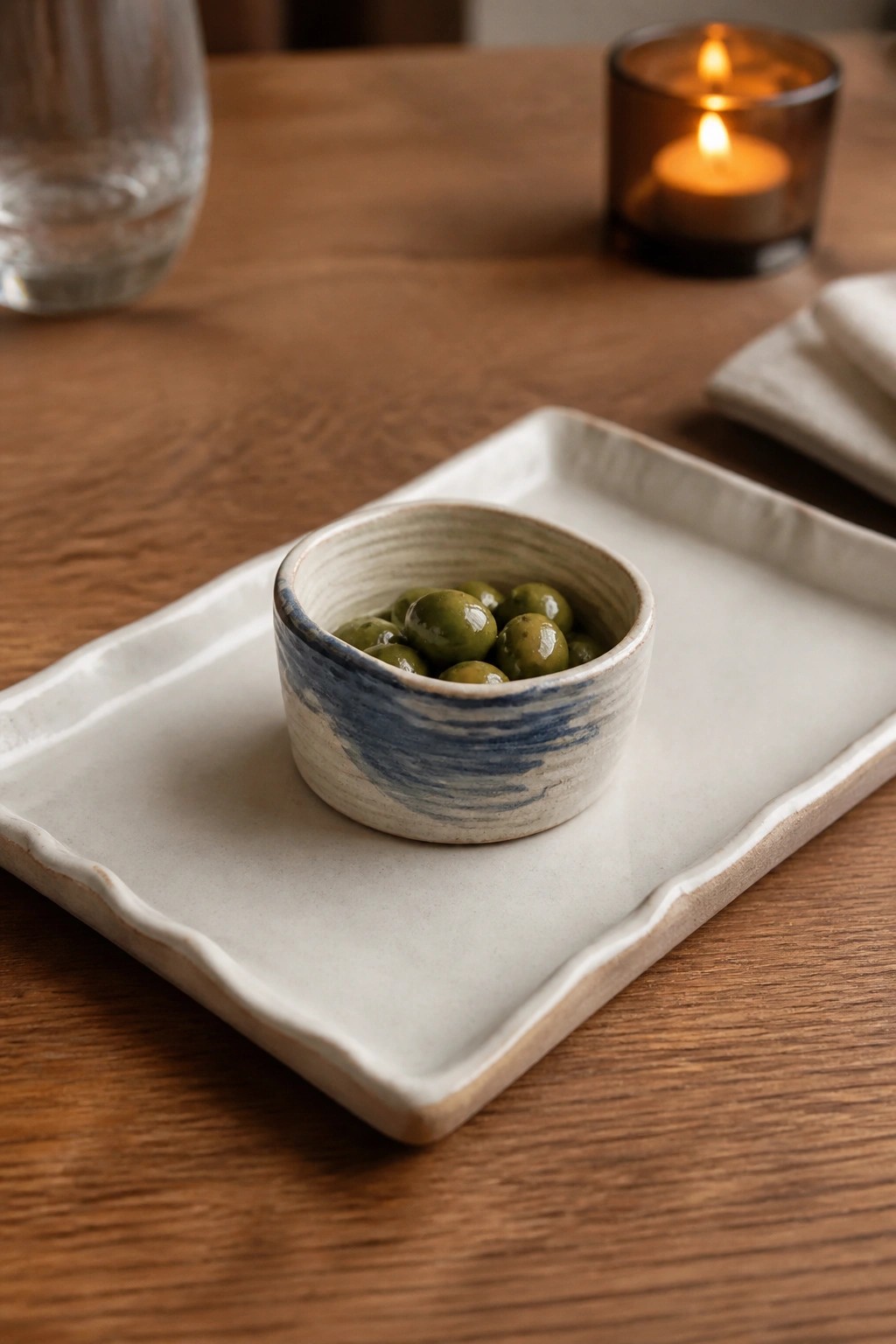 Green olives in a blue-swirled bowl on a white rectangular tray on wood