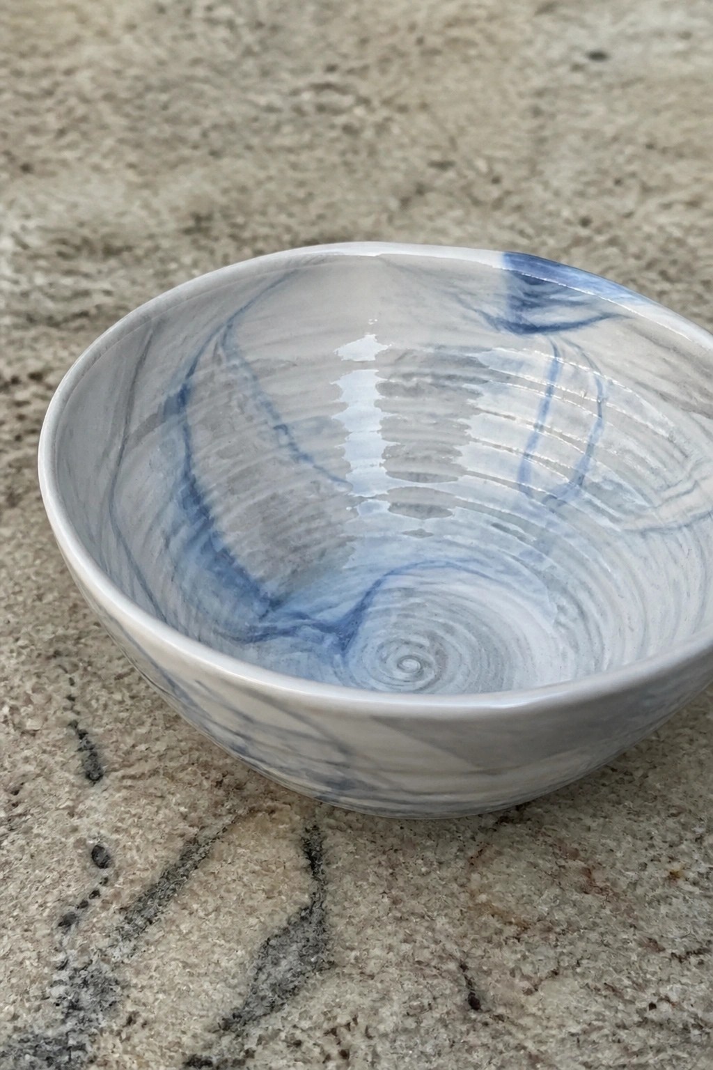 Ceramic bowl with blue and white marbled glaze on textured stone surface