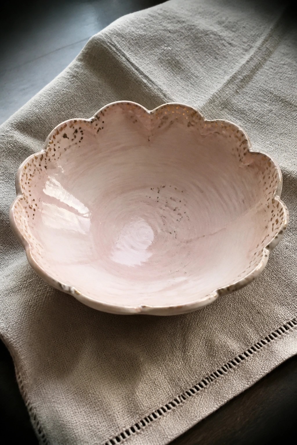 Pale pink scalloped ceramic bowl with gold speckles on beige linen cloth