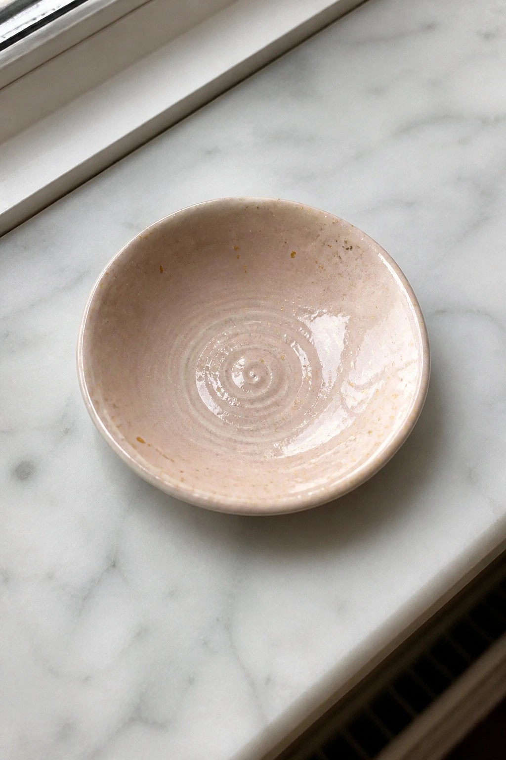 Small pink ceramic bowl with spiral glaze on white marble surface