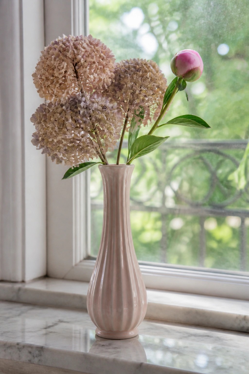 Pink ribbed vase with dried hydrangeas and peony bud on marble windowsill