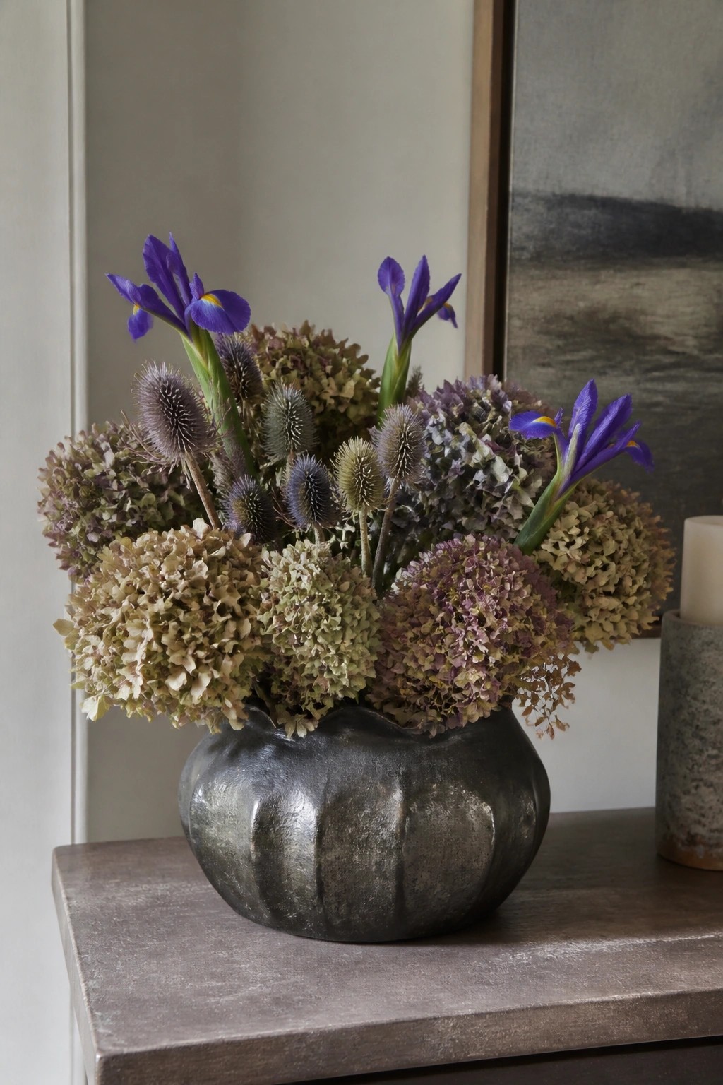 Purple irises and dried hydrangeas in a dark metallic vase on wood
