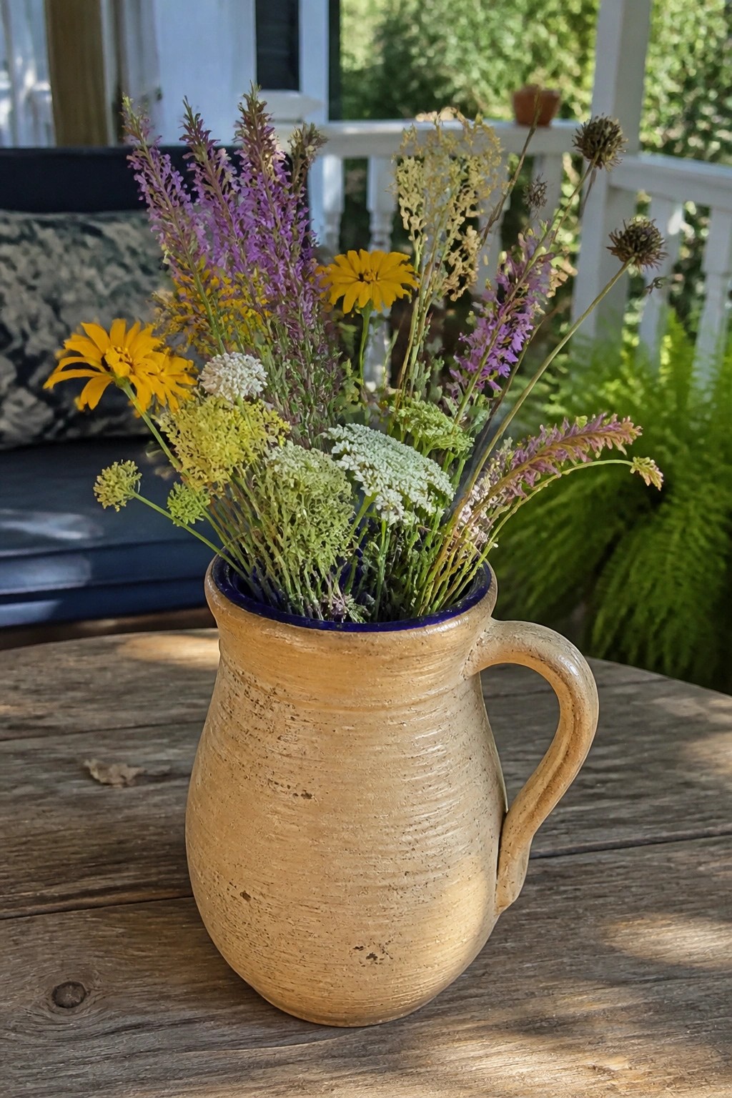 Rustic earthenware pitcher with blue rim holding colorful wildflowers on wooden table