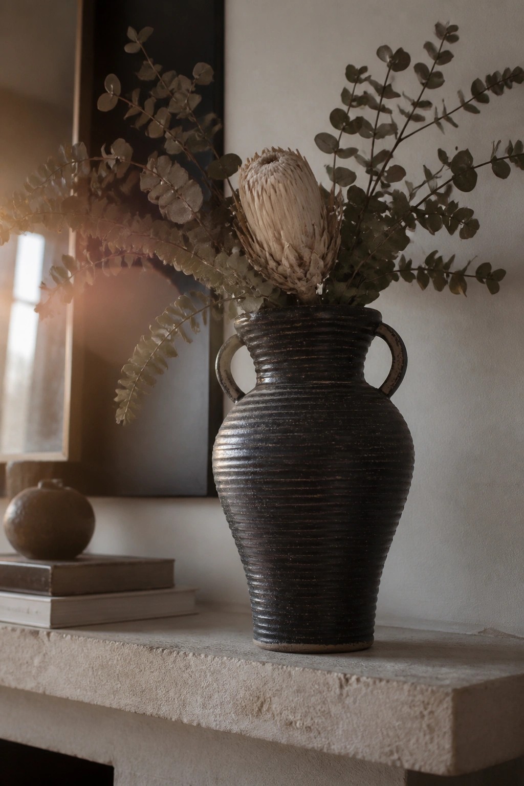 Dark ribbed vase with dried protea and eucalyptus on stone mantel.
