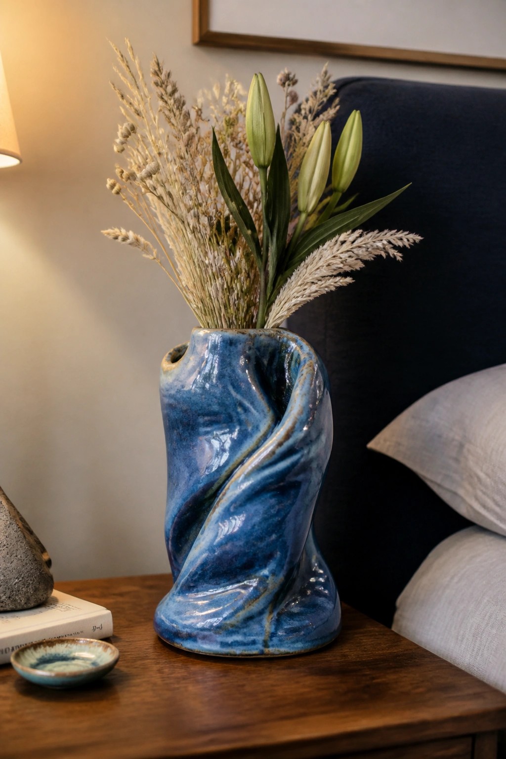 Blue twisted ceramic vase with dried grasses and green lily buds on wood table