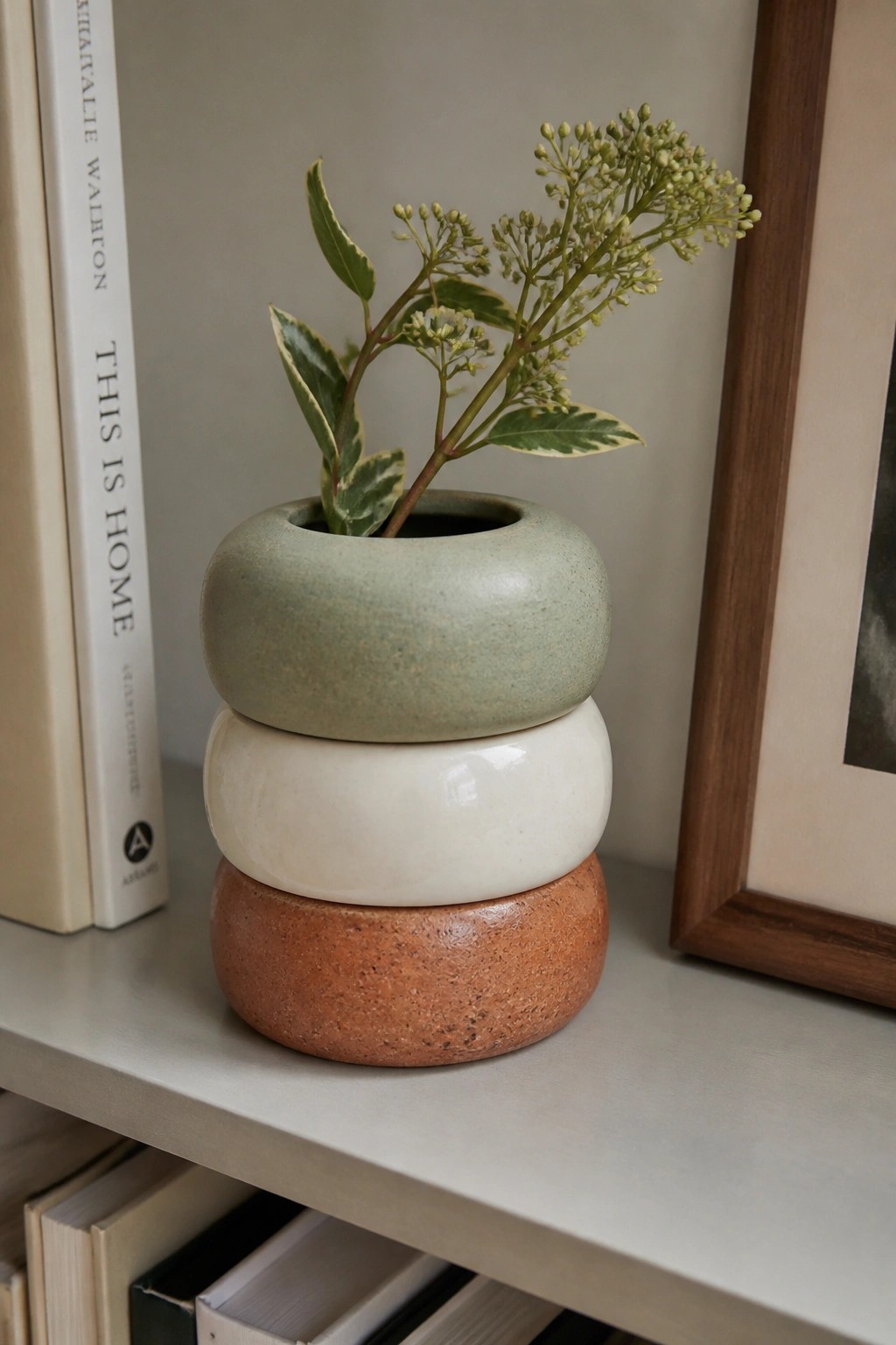 Stacked ceramic vase in sage green, white, and terracotta with leafy plant on shelf