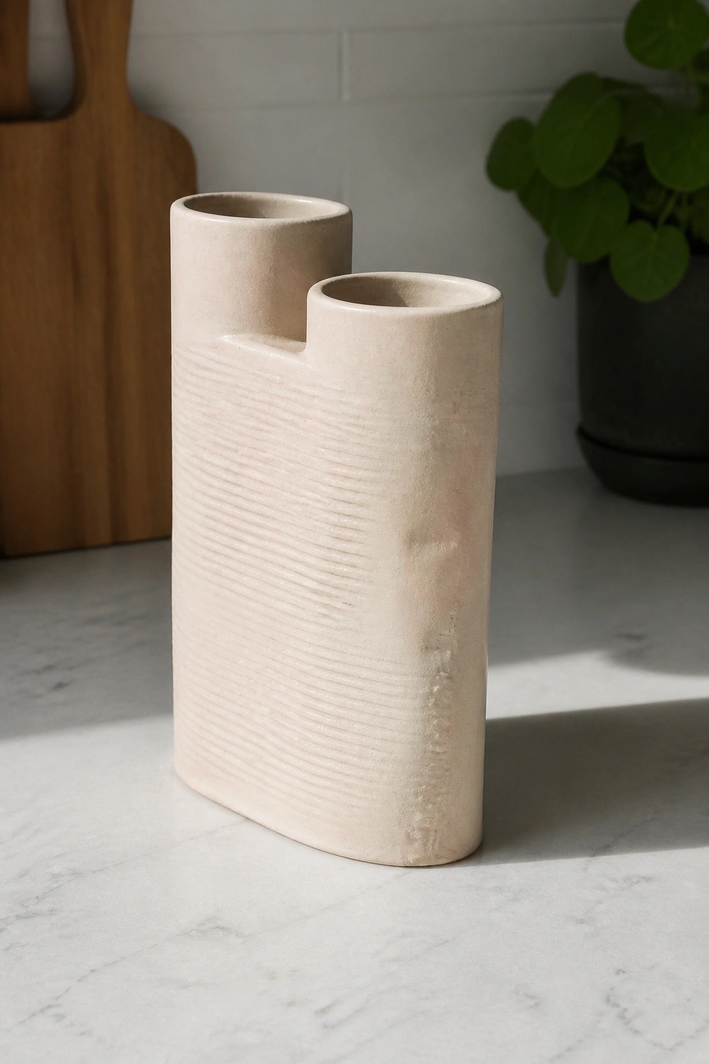 Beige ceramic double-spout vase with horizontal ridges on marble countertop.