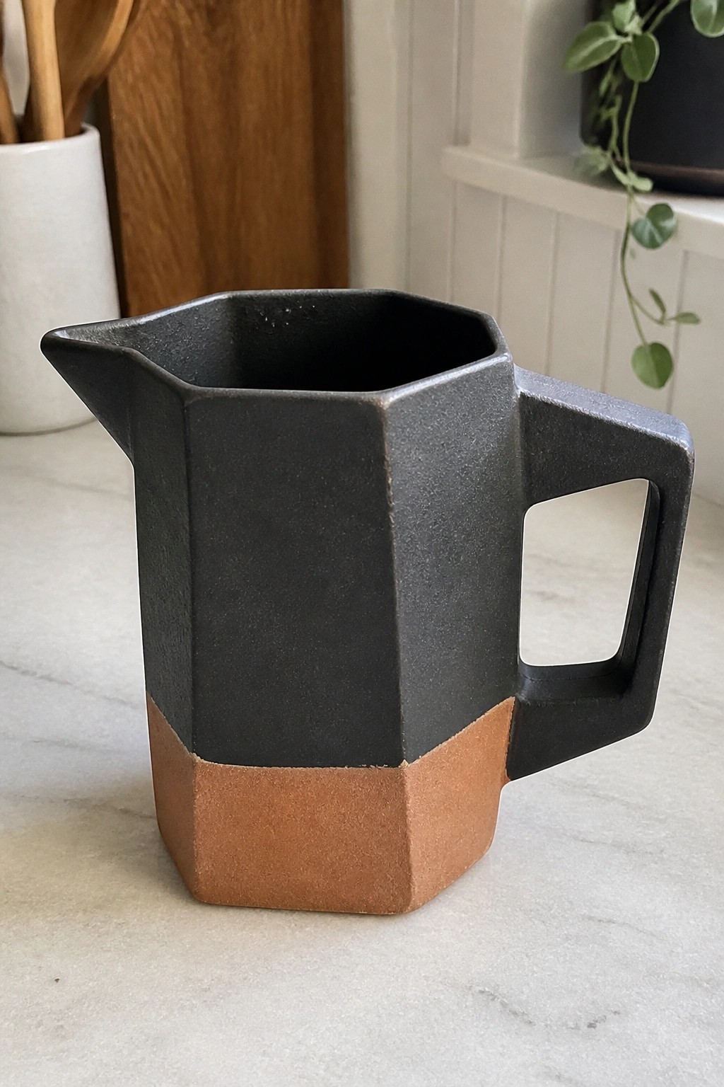 Faceted black and terracotta ceramic pitcher with square handle on marble counter