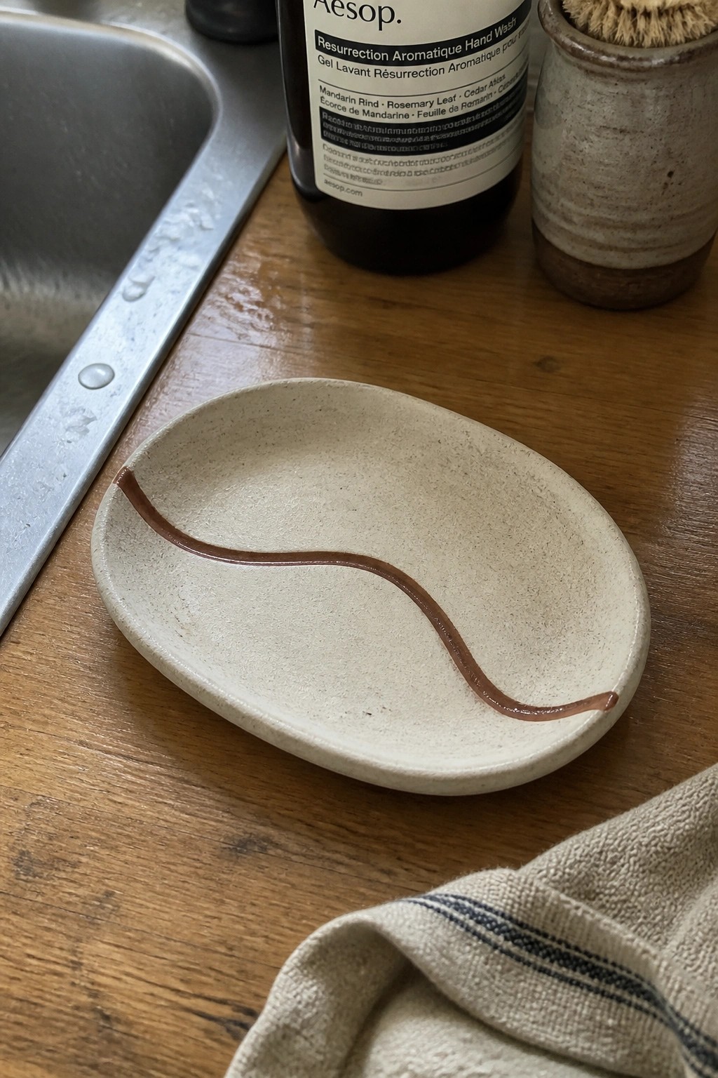 Oval ceramic dish with wavy brown line on wooden counter near sink