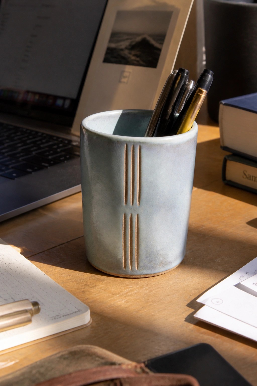 Light blue ceramic pen holder with pens on sunlit wooden desk.