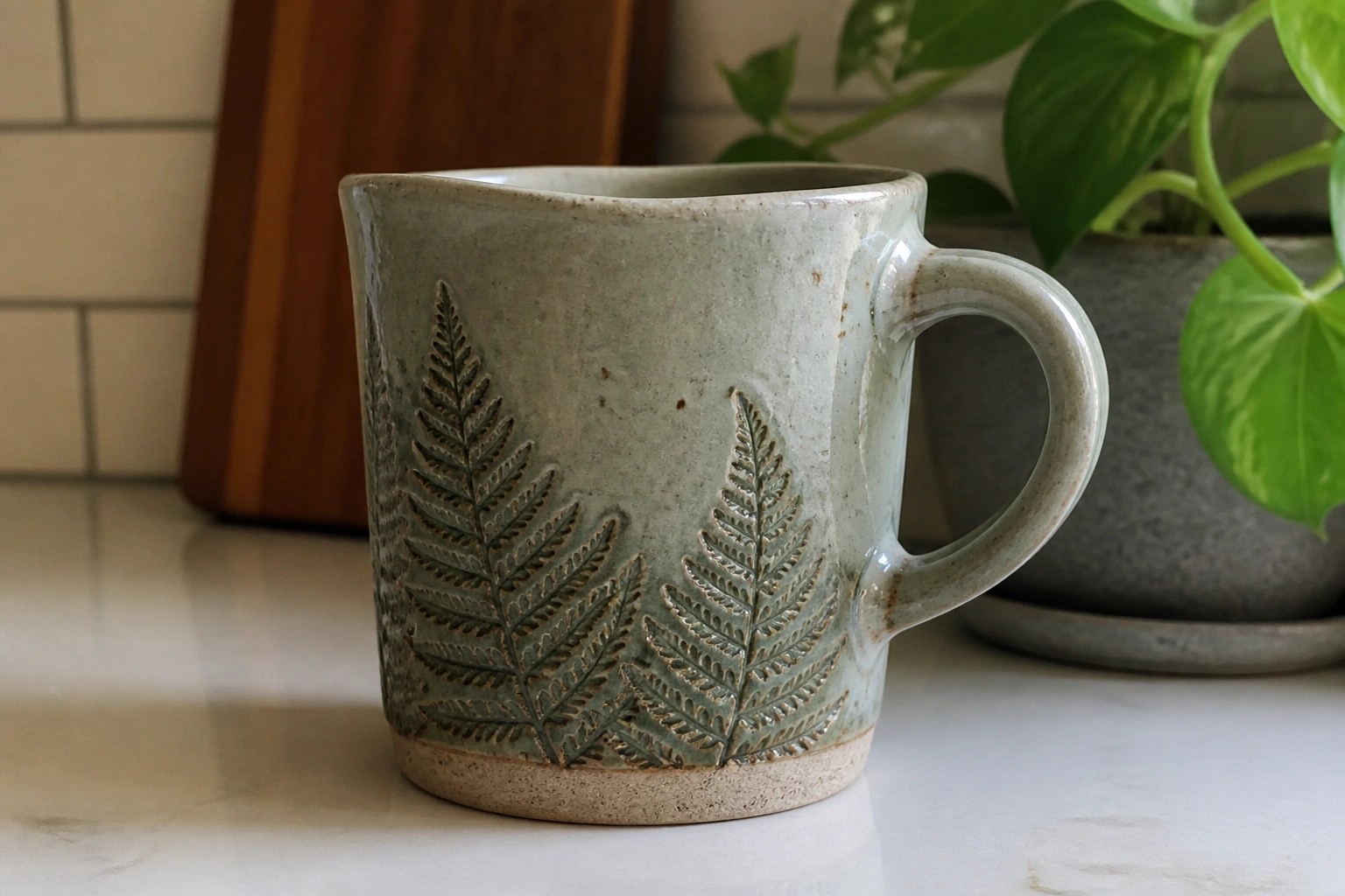 Green ceramic mug with embossed fern leaves on marble countertop