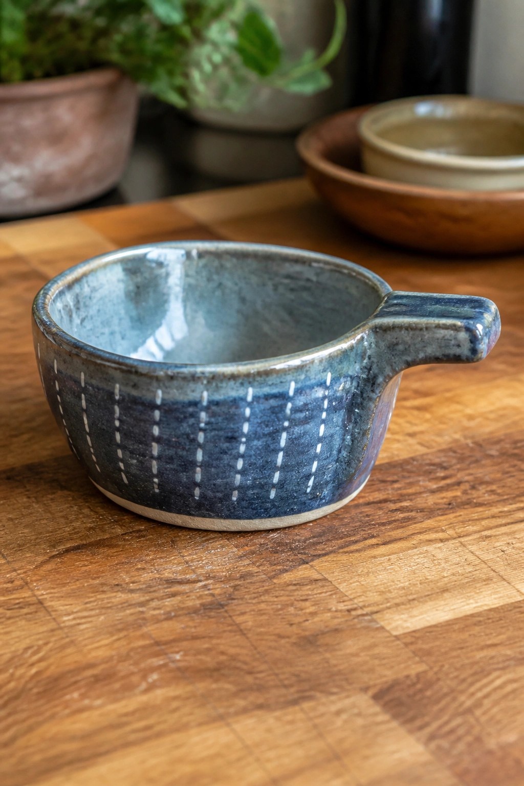 Blue ceramic bowl with white dashes and handle on wooden table