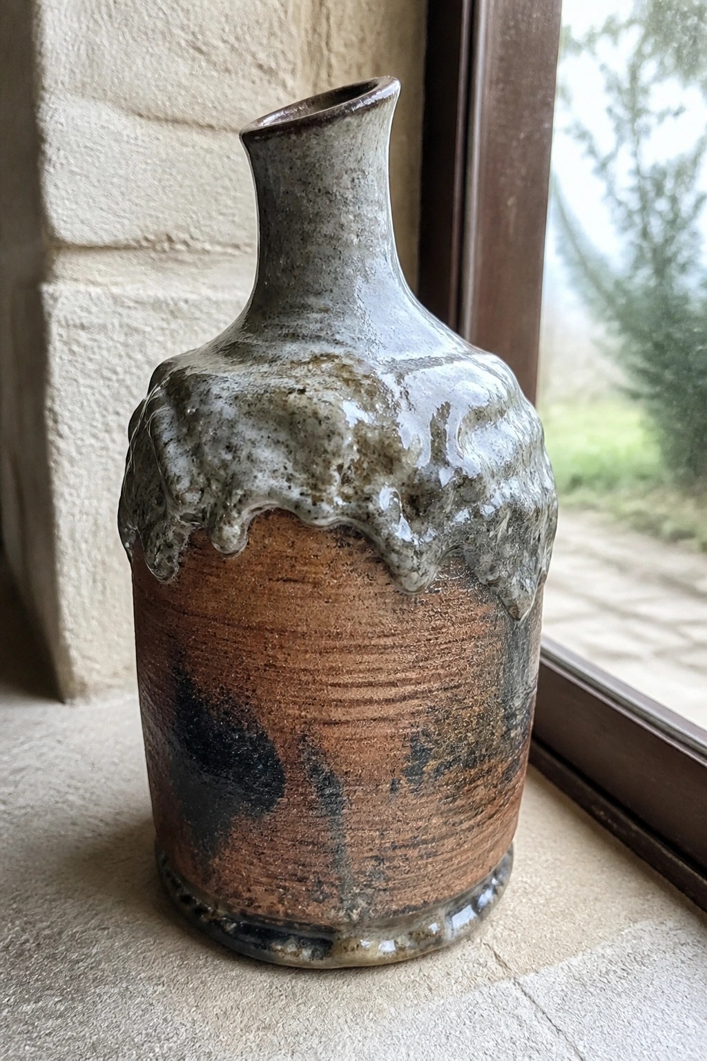 Rustic ceramic vase with dripping gray-white glaze on a sunlit windowsill