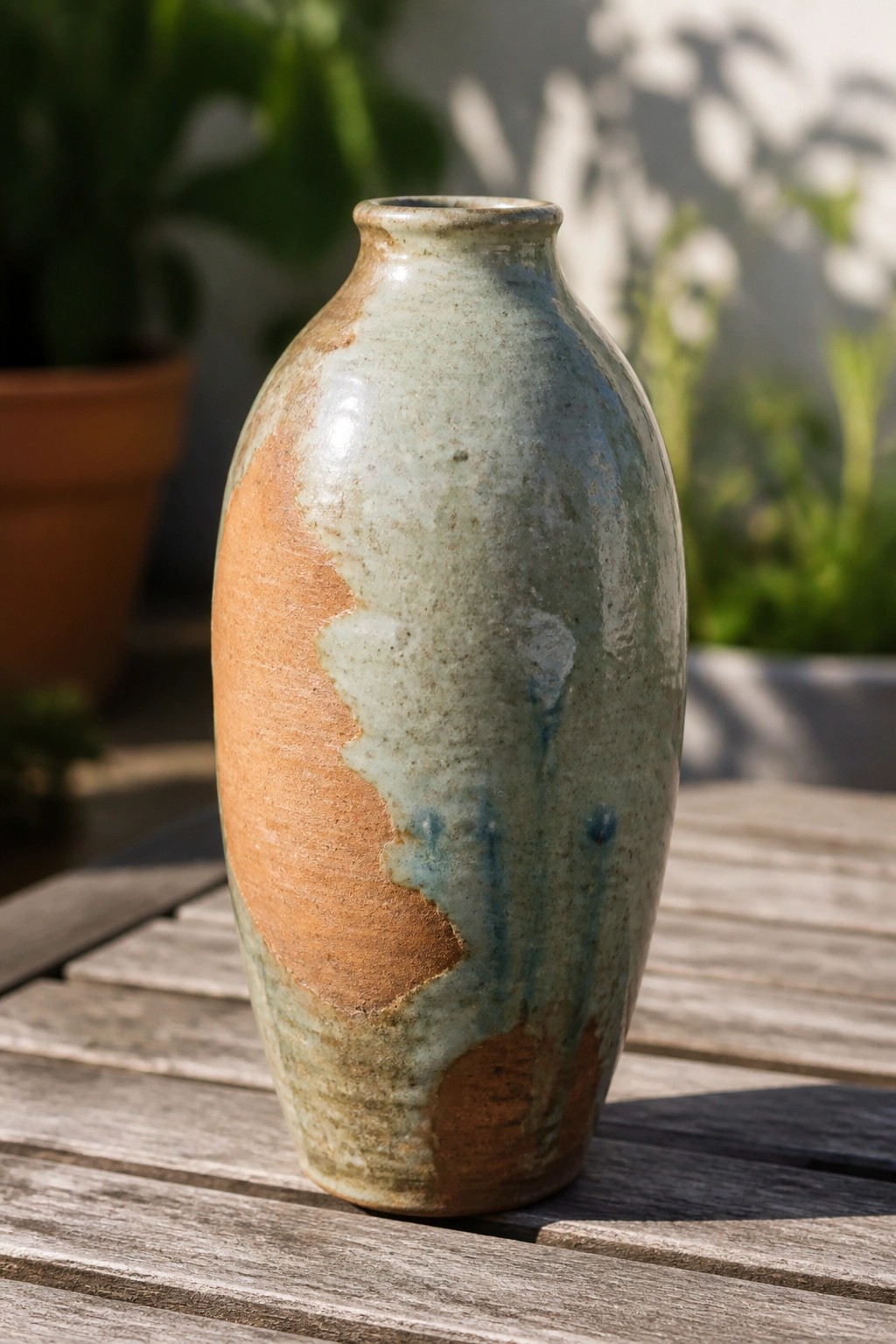 Rustic ceramic vase with mottled blue-green and brown glaze on wooden table outdoors