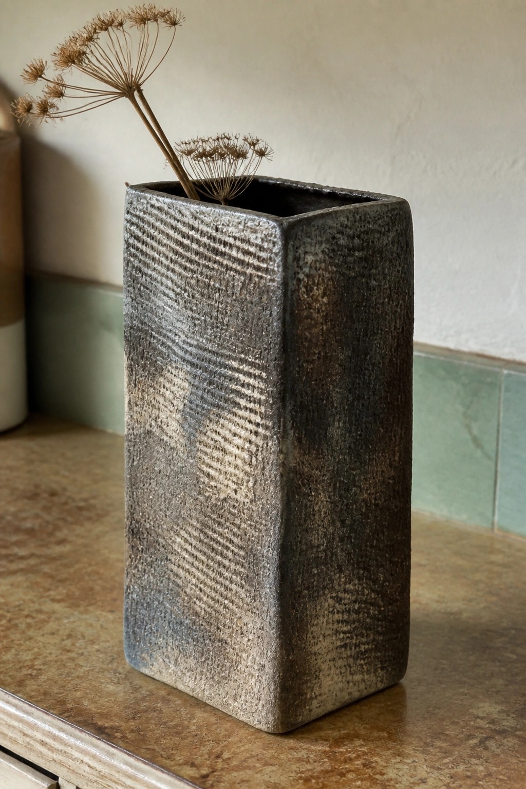Rectangular textured gray ceramic vase with dried flower stems on marble counter