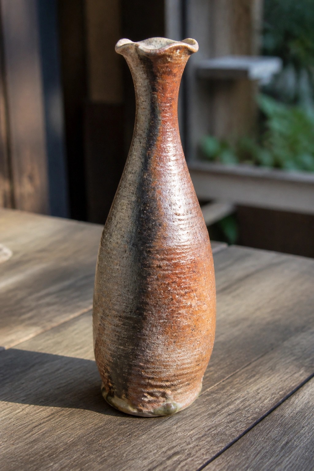 Rustic ceramic vase with brown-orange glaze and wavy rim on wooden table
