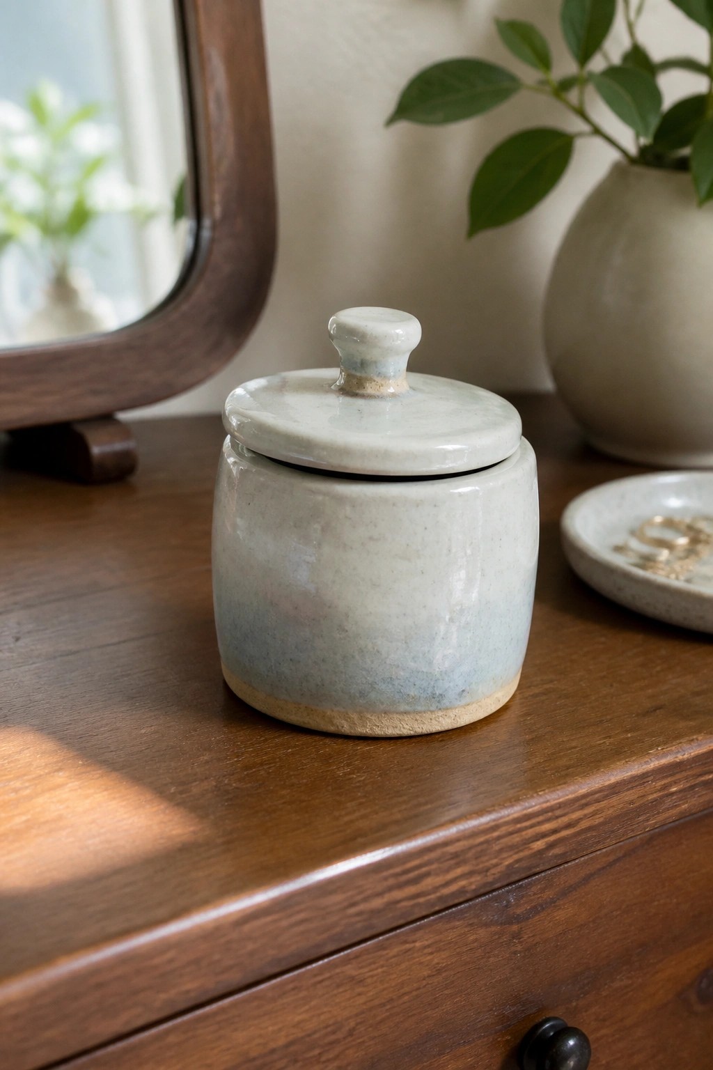 Ceramic lidded jar with blue glaze on wooden dresser beside mirror and plant