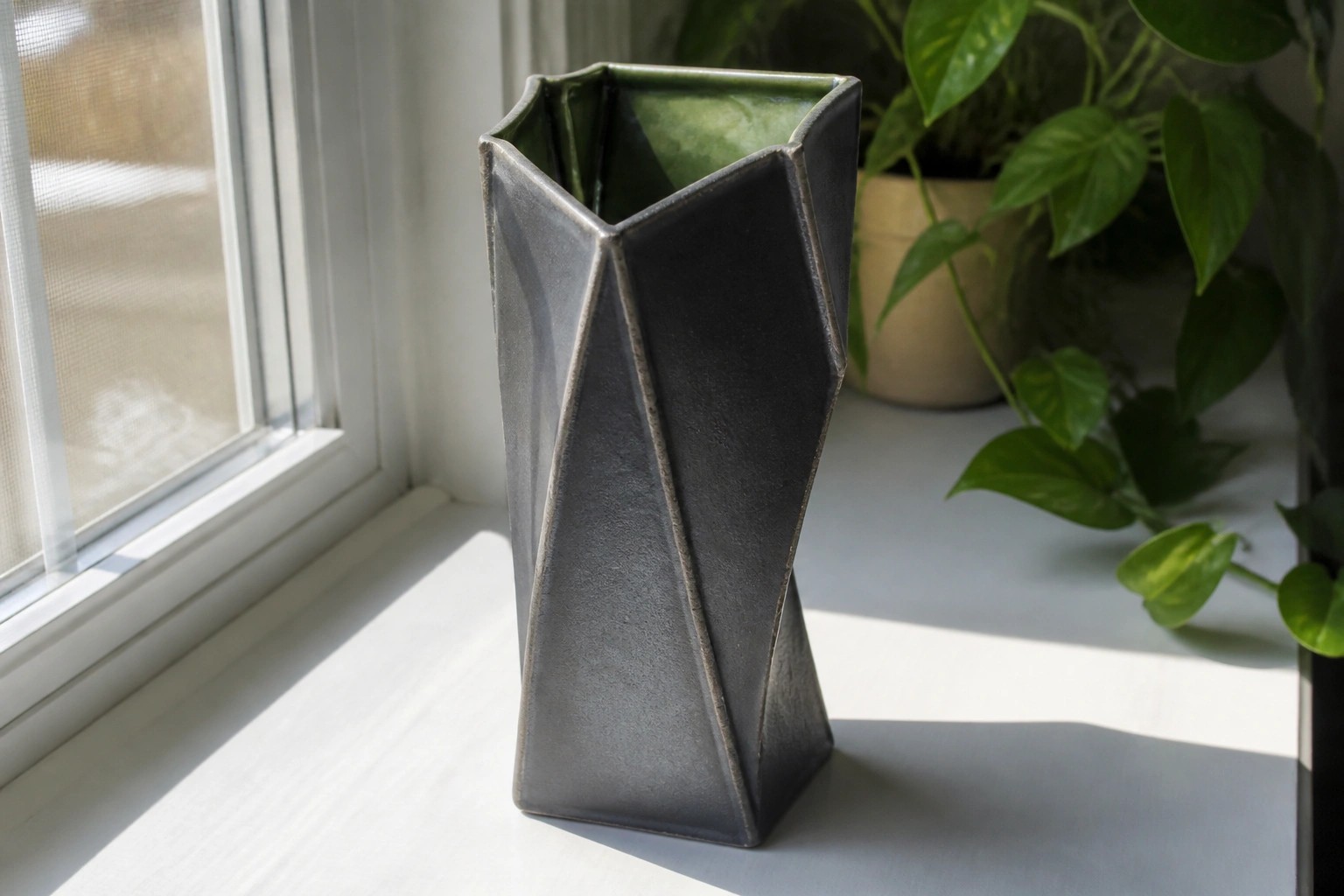 Black angular faceted vase with green interior on a sunny windowsill.
