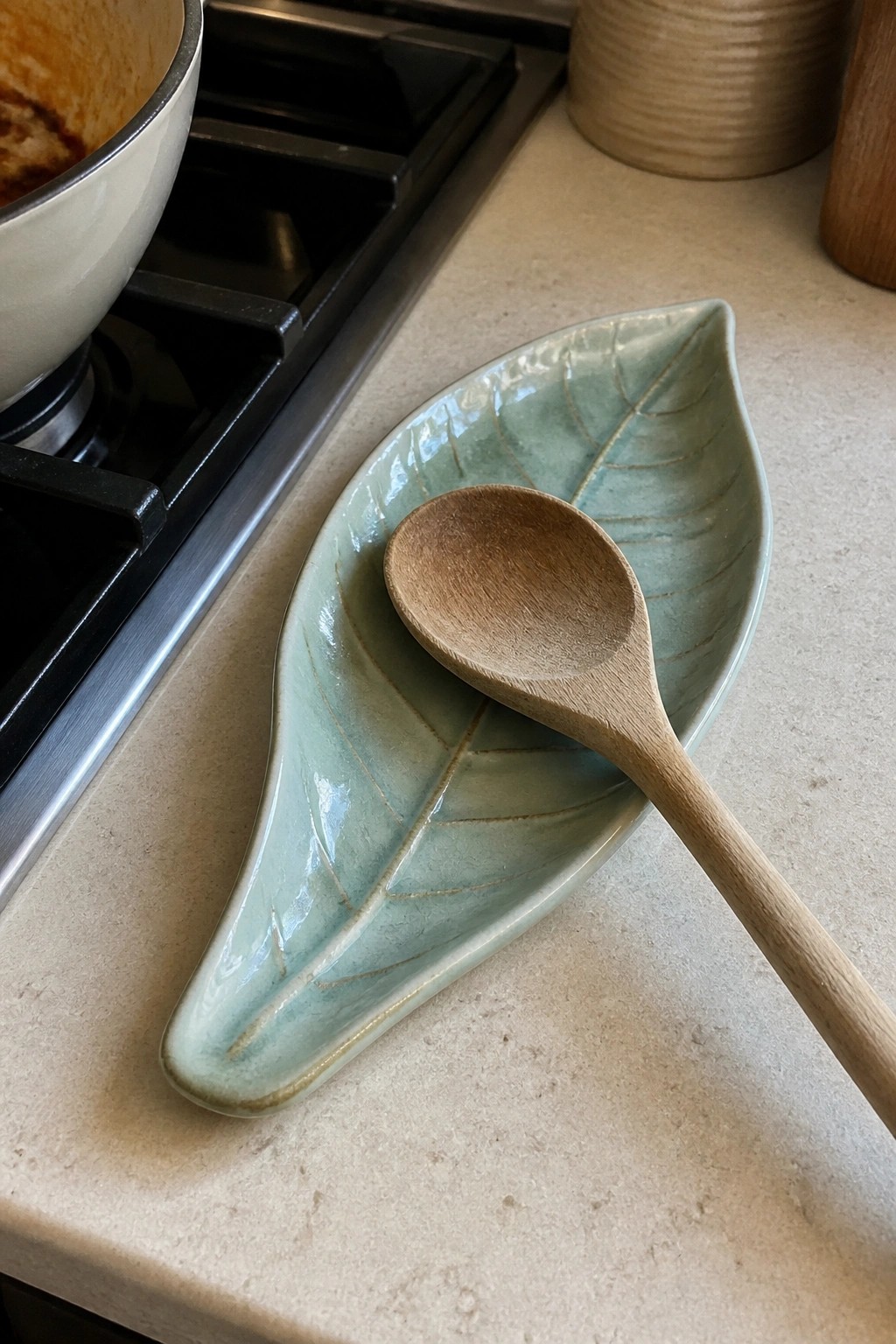 Wooden spoon resting on light green leaf-shaped ceramic dish on kitchen counter