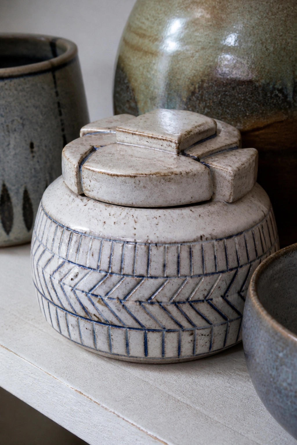 Lidded ceramic jar with blue herringbone pattern among other pottery on a shelf.