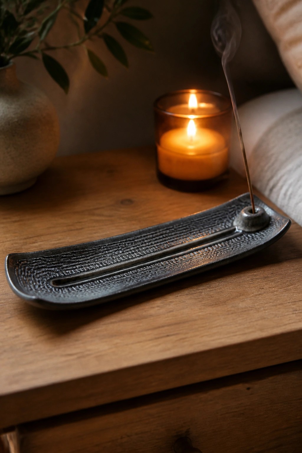 Burning incense stick with rising smoke beside lit candle on wooden table