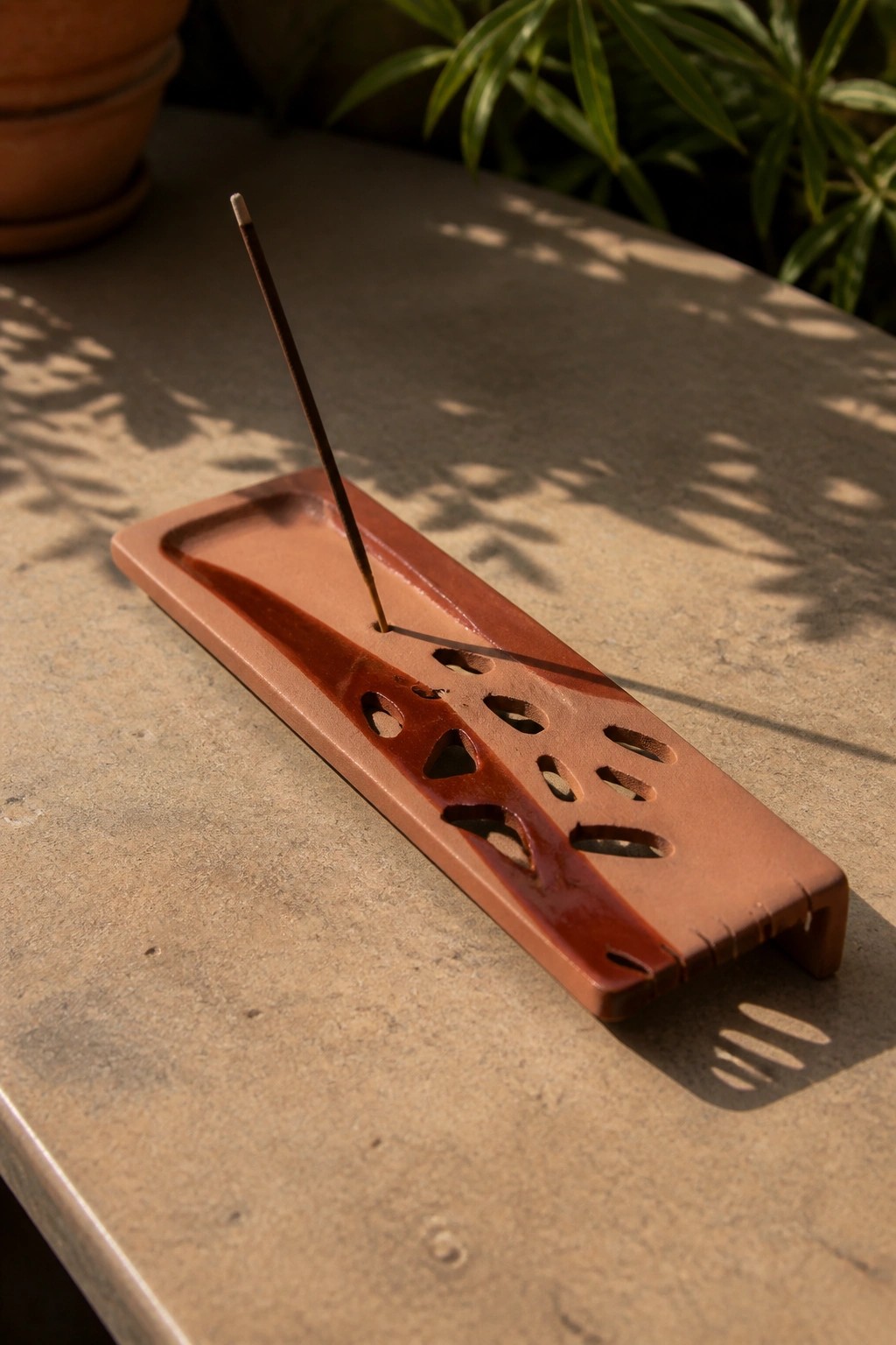 Terracotta incense holder with stick on stone table amid plant shadows